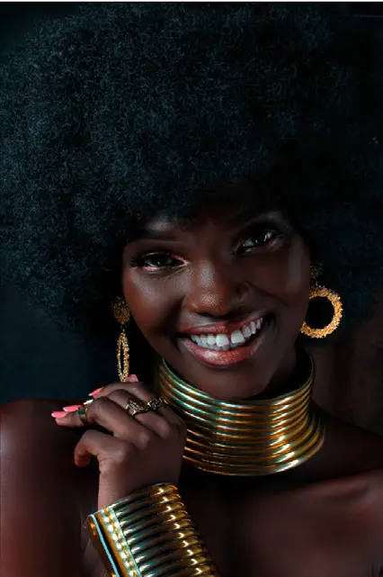 A woman smiling broadly, wearing stacked gold neck rings