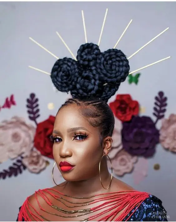 A woman with sculpted braided hair against a floral backdrop