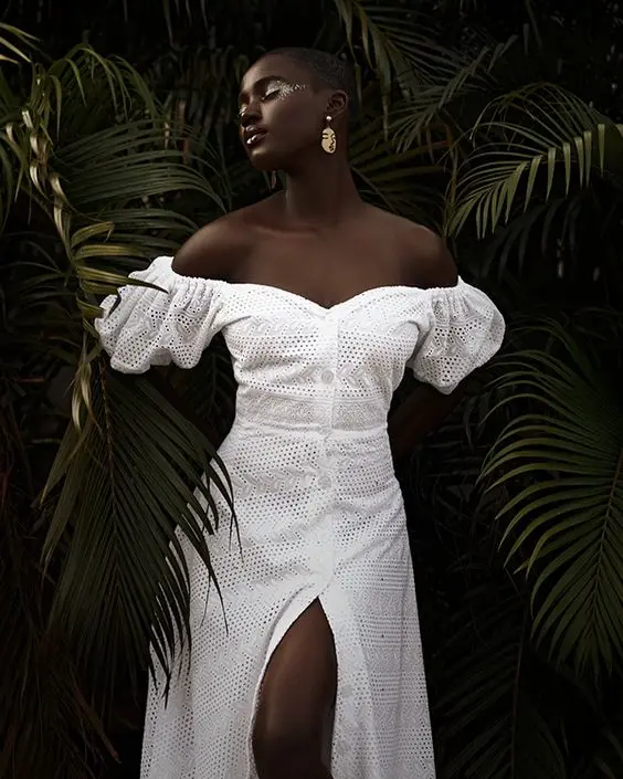 A woman in a white dress standing among dark tropical leaves