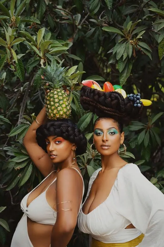 Two women side by side, one carrying a basket of fruit on her head