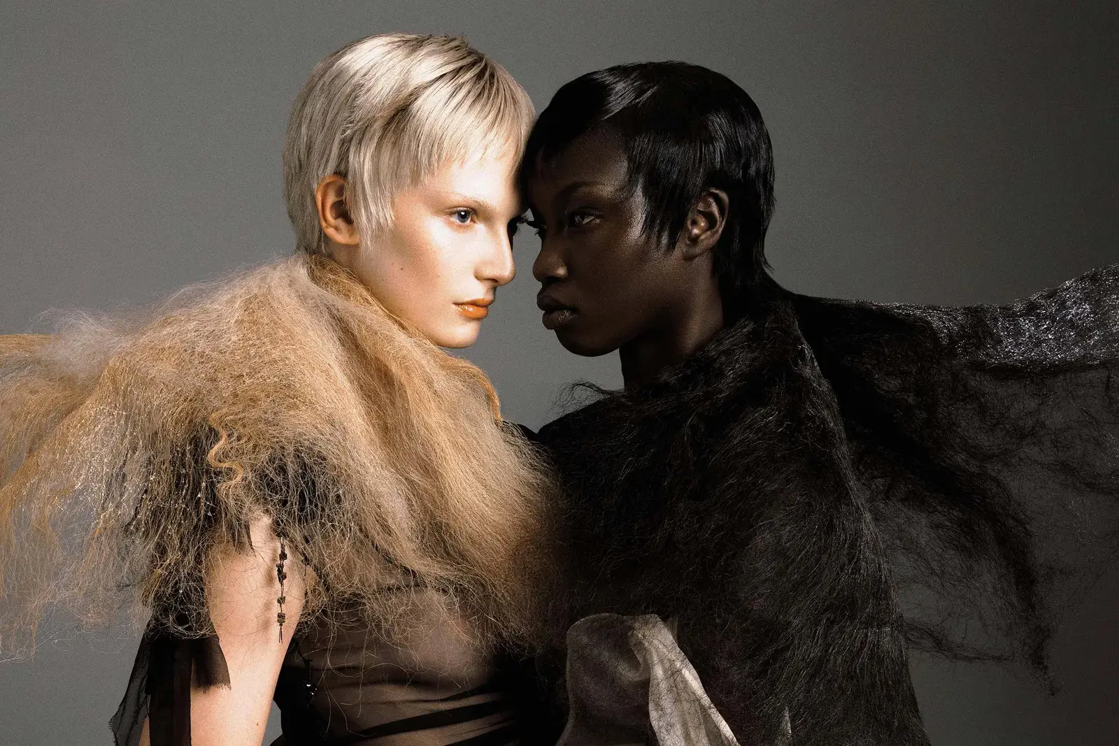 Two models, one fair and one dark-skinned, foreheads touching in an editorial portrait